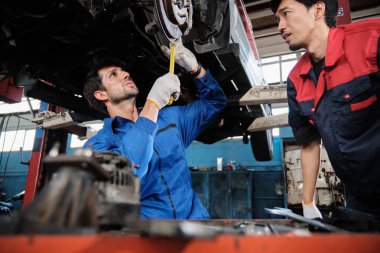 İki erkek tamirci işbirliği yapıyor, Latin ve Asyalı işçiler otomotiv tekerleklerini tamir ediyor ve garaj istasyonunda araba süspansiyonlarını koruyor, ve araç taşımacılığı sektöründe teknisyen mühendisliği hizmeti veriyor..