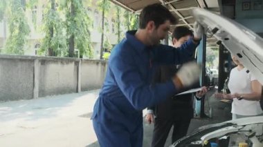 Kadın müşteri ve Asyalı erkek müdür, EV otomobil tamirhanesinde teknisyen motor tamirciliği, akü tamirciliği, müşteri hizmetleri bakımı ve ulaşım sektörü konularında görüştü..