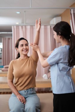 İspanyol kadın hasta kol esneme, tedavi, omuz kası ağrısı, Asyalı fizyoterapist tarafından tedavi, pasif tıbbi tedavi, sağlık masajı, spa kliniği.