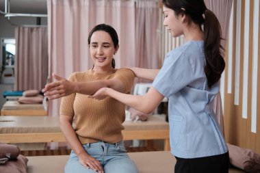 İspanyol kadın hasta kol esneme, tedavi, omuz kası ağrısı, Asyalı fizyoterapist tarafından tedavi, pasif tıbbi tedavi, sağlık masajı, spa kliniği.