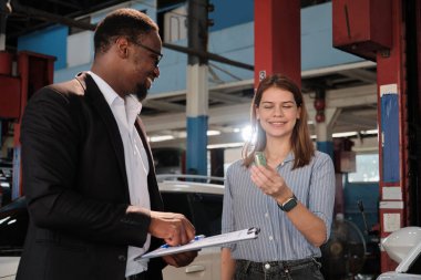 Garanti araçları servis işi, beyaz kadın müşteri araba anahtarını siyah erkek sigorta acentesinden alarak mutlu, tadilat bittikten sonra otomotiv garajı istasyonunda tamir ve bakım..