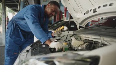 EV araba kontrolü, siyah erkek tamirci sabit otomobil garaj istasyonunda elektrik motoru ve pil hizmetini denetliyor ve koruyor, profesyonel teknoloji taşımacılığı sektörü.