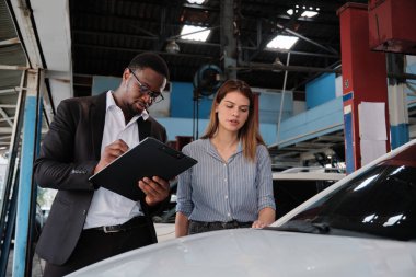 Garanti hizmeti işi, beyaz kadın müşteri araba boyasını inceliyor ve siyah erkek sigorta acentesiyle tırmalama onarımı yapıyor, araba taleplerini kabul ediyor, araba tamirhanesinde tamirat ve bakım yapıyor..