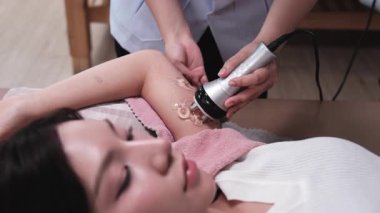 Asyalı kadın hasta yağ selülit azaltımı, kozmetoloji prosedürü için kolunda ultrason cihazıyla fizyoterapist, güzellik uzmanı ve sağlık spa merkezinde tıbbi tedavi görüyor..