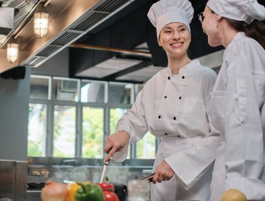 Önlüklü iki beyaz kadın aşçı birlikte yemek pişiriyor. Lezzetli yemeklerde profesyonel gurme partnerler, otel yemeklerinde malzeme hazırlığı ve aşçılık yemekleri..