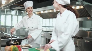Önlüklü iki beyaz kadın aşçı birlikte yemek pişiriyor. Lezzetli yemeklerde profesyonel gurme partnerler, otel yemeklerinde malzeme hazırlığı ve aşçılık yemekleri..