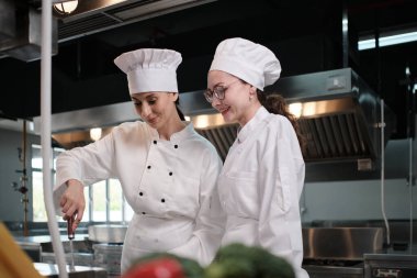 Önlüklü iki beyaz kadın aşçı birlikte yemek pişiriyor. Lezzetli yemeklerde profesyonel gurme partnerler, otel yemeklerinde malzeme hazırlığı ve aşçılık yemekleri..