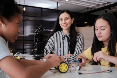 Beyaz bayan öğretmen, ilkokul öğrencilerine, fen sınıfında öğrenim masasında robotik silah tasarımına ve ilkokul öğrencileri için deney bilgilerine danışmanlık yapar ve talimat verir..