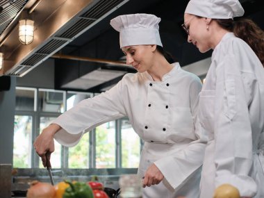 Önlüklü iki beyaz kadın aşçı birlikte yemek pişiriyor. Lezzetli yemeklerde profesyonel gurme partnerler, otel yemeklerinde malzeme hazırlığı ve aşçılık yemekleri..