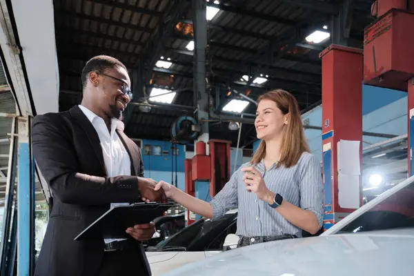 Garanti araçları servis işi, beyaz kadın müşteri araba anahtarını siyah erkek sigorta acentesinden alarak mutlu, tadilat bittikten sonra otomotiv garajı istasyonunda tamir ve bakım..