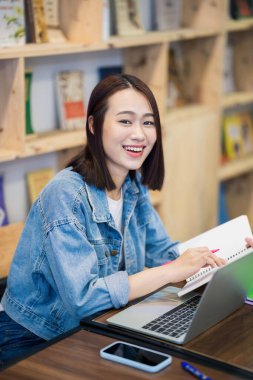 Genç Asyalı kız kütüphanede okuyor.