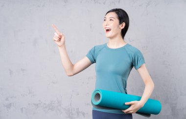 Elinde yoga halısı tutan genç bir Asyalı kadın.