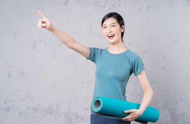 Elinde yoga halısı tutan genç bir Asyalı kadın.