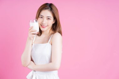 Pembe arka planda süt içen Asyalı genç bir kadın resmi