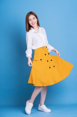 Mavi arka planda genç Asyalı bir kadının tam boy fotoğrafı.