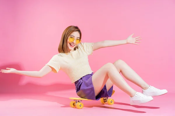 照片上的亚洲少女带着粉色背景的滑板 — 图库照片