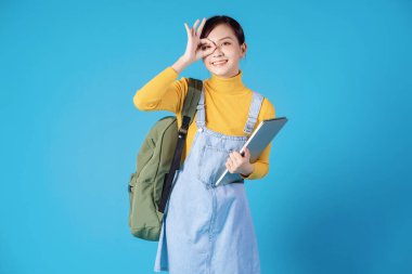 Genç Asyalı öğrenci mavi arka planda poz veriyor