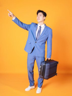 Arka planda bavulu tutan Asyalı genç bir iş adamı resmi