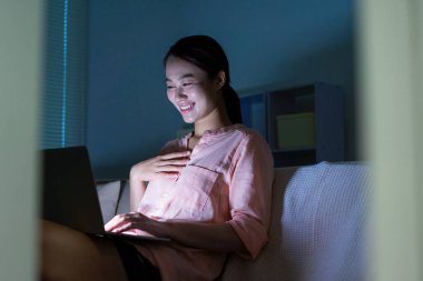 Genç Asyalı kadının gece yarısı karanlıkta dizüstü bilgisayar kullanırken fotoğrafı.