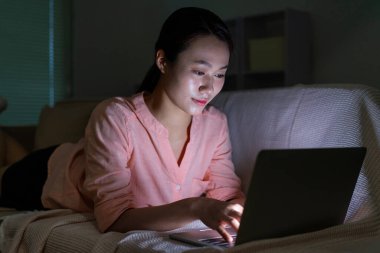 Genç Asyalı kadının gece yarısı karanlıkta dizüstü bilgisayar kullanırken fotoğrafı.