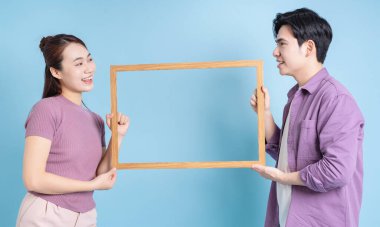 Genç Asyalı çift mavi arkaplanda fotoğraf çerçevesi tutuyor.