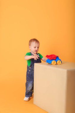 Küçük yakışıklı bir çocuk açık renkli bir puffe üzerinde bir oyuncakla oynuyor. Sarı arka planda bir çocuğun stüdyo çekimi..