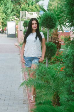 Sokakta, palmiye ağaçlarının arasında boylu poslu esmer bir kadın. Tropik iklimde bir kızın portresi .