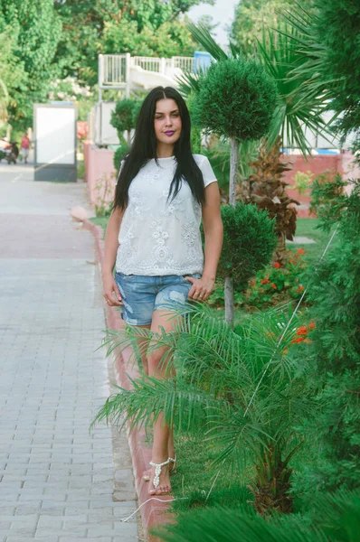 Sokakta, palmiye ağaçlarının arasında boylu poslu esmer bir kadın. Tropik iklimde bir kızın portresi .