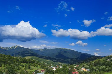 Dağlar dağ köyünün ovalarında ormanlarla kaplıdır. Güneşli bir günde bulutlarla kaplı kırsal dağlar..