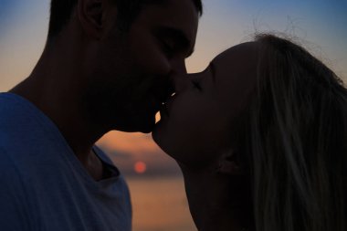 Genç bir çiftin silueti, gün batımına ya da gün doğumuna karşı. Deniz kıyısında ya da okyanusta bir kadın ve erkeğin silueti..