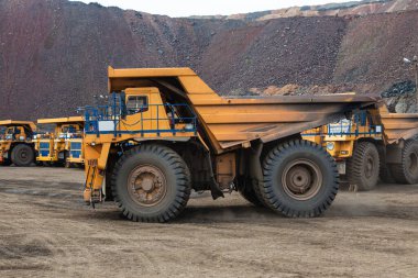 Large yellow dump trucks engaged in the transportation of rock mass in the quarry for mining. Machinery and equipment for iron ore mining