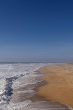 Okyanus ve sahilin dikey görüntüsü berrak bir gökyüzünün altında.