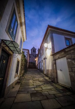 Sonunda bir kilise kulesi olan bir cadde. Taş zemin ve her iki tarafında da eski binalar olan bir cadde.