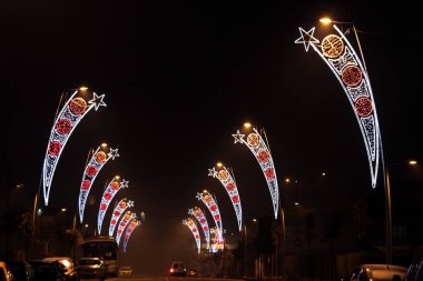 Noel ışıklarıyla süslenmiş bir caddedeki tüm sokak lambaları geceyi aydınlatıyor.