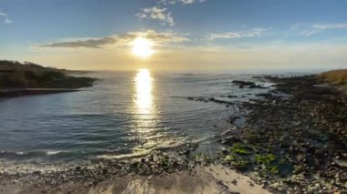 Denizin üzerinde gün batımı gelir, ve sahilde sakin bir gelgit.