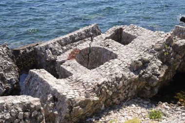 Kristal berrak denizin yanındaki antik bir taş binanın kalıntıları. Turkuaz suyun arka planına karşı tarihin ve doğanın atmosferi.