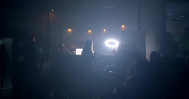 Siyah bir arka planda, gece kulübünün arka planında yuvarlak bir lambanın önünde duran insanların siluetleri. Odada dolaşıyorlar, kırmızı ışık. Ortamı sakinleştir. CZ, Prag, Republici, 28.10.22