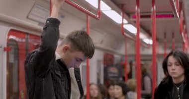 Yolcu metro korkuluğuna tutunuyor. İnsanlar çıkışa gidiyor, o ayakta duruyor. Telefonun toplu taşımada kullanımı. CZ, Prag, Veleslavin, 1.10.22 