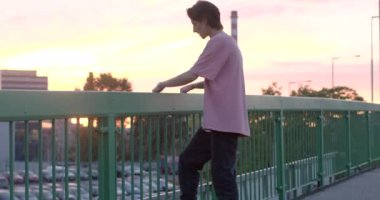 Adam şehirdeki köprünün korkuluklarına tırmanıyor. Bacağını korkuluklardan sallıyor. Hayata karşı tehlike. CZ, Prag, Radlicka 30.9.22.