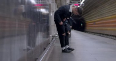 The guy sits on the curb of the metro station, waiting for the train. The train arrives at the platform, opens the doors. The movement of passengers at the station. CZ, Prague, Veleslavin, 1.10.22 