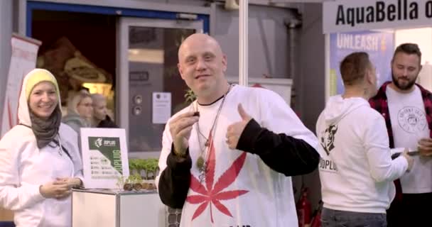 大麻の苗を持つ男は トレードショーで手のジェスチャーのように示しています 健康と健康のためのCbdを販売する事業を設立する会社 2023レターニー プラハ — ストック動画