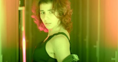 Portrait of a girl in blue and red light. She moves her body, touches the wall. He holds his shirt on his elbows with his hands. The head turns to the sides.