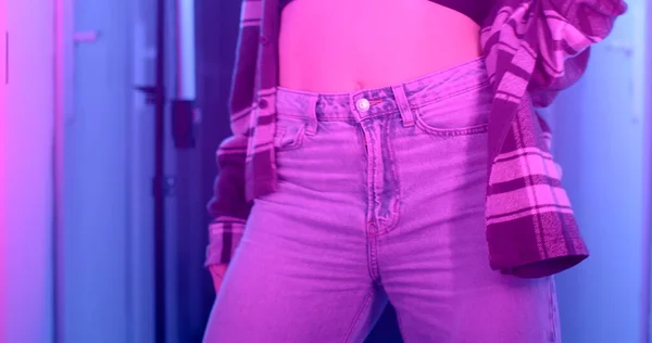 Legs with body in jeans dance in flashing light. She opens her body from the clothes, moves her hand into the camera. Against the background of a corridor in bokeh.