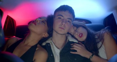 Transportation of passengers in the back seat of a taxi. Polyamorous guy with two girls, focus of attention, open flirting. He will cover his face with his hands - attention fatigue.