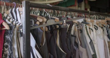 Atölyedeki kıyafetlerin tamiri. Askıda bir sürü kıyafet var. Sıraya dizilmiş yoğun bir kıyafet akıntısı. Kumaş tozu, alerji..