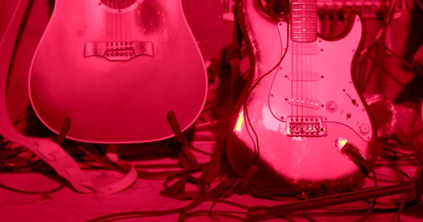 The musicians guitars stand in red light on the stage. Coiled wires with plugs. Preparing equipment for use in a concert. CZ, Prague, Zizkov, 10.12.22.