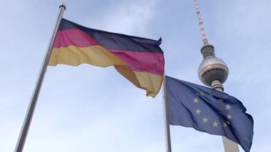 Flags of Germany and EU flutter in wind against sky and landmarks. Symbols of democratic, social, legal state. 