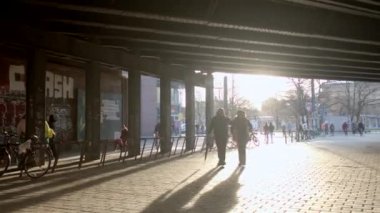 The movement of pedestrians and cyclists under the bridge in the city. The light of the sun, a glare of light on the sidewalk. Shadows and silhouettes movement. DE, Berlin, Friedrich, 16.1.2023. 