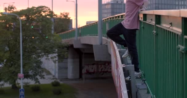 彼は下を見る 彼は手の男の髪をまっすぐに橋の上に立って 彼の手で手すりを保持しています 日没の光の中で街の背景に プラハ ヴルタフスカ — ストック動画