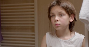 Cutting off sticky hair with chewing gum in a boy. He cuts off a curl of stuck hair with scissors, looks in the mirror, tries on the device. The guy is upset.